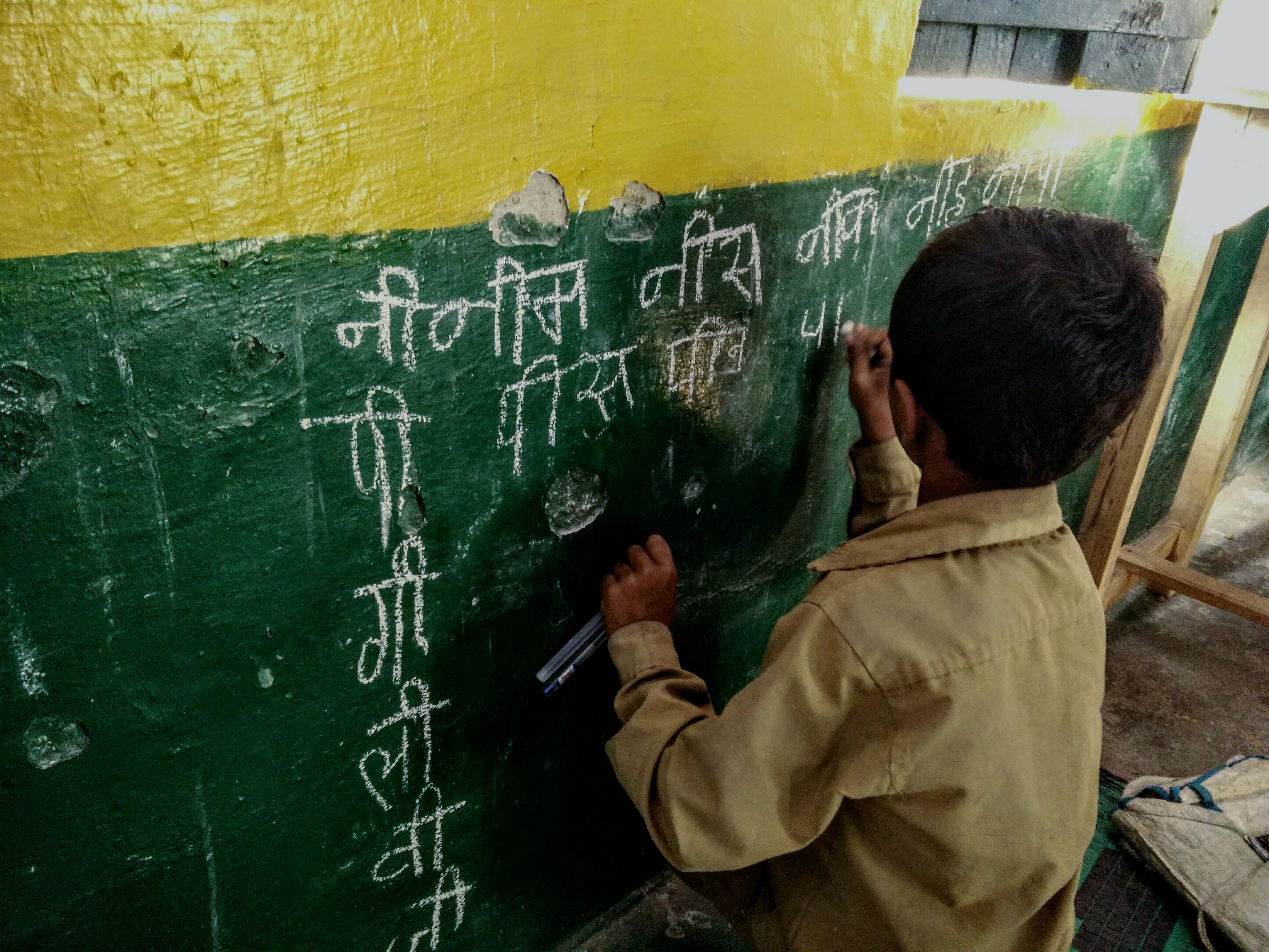 A child uses chalk to write on the wall during a TaRL reading activity in Karnataka, India.